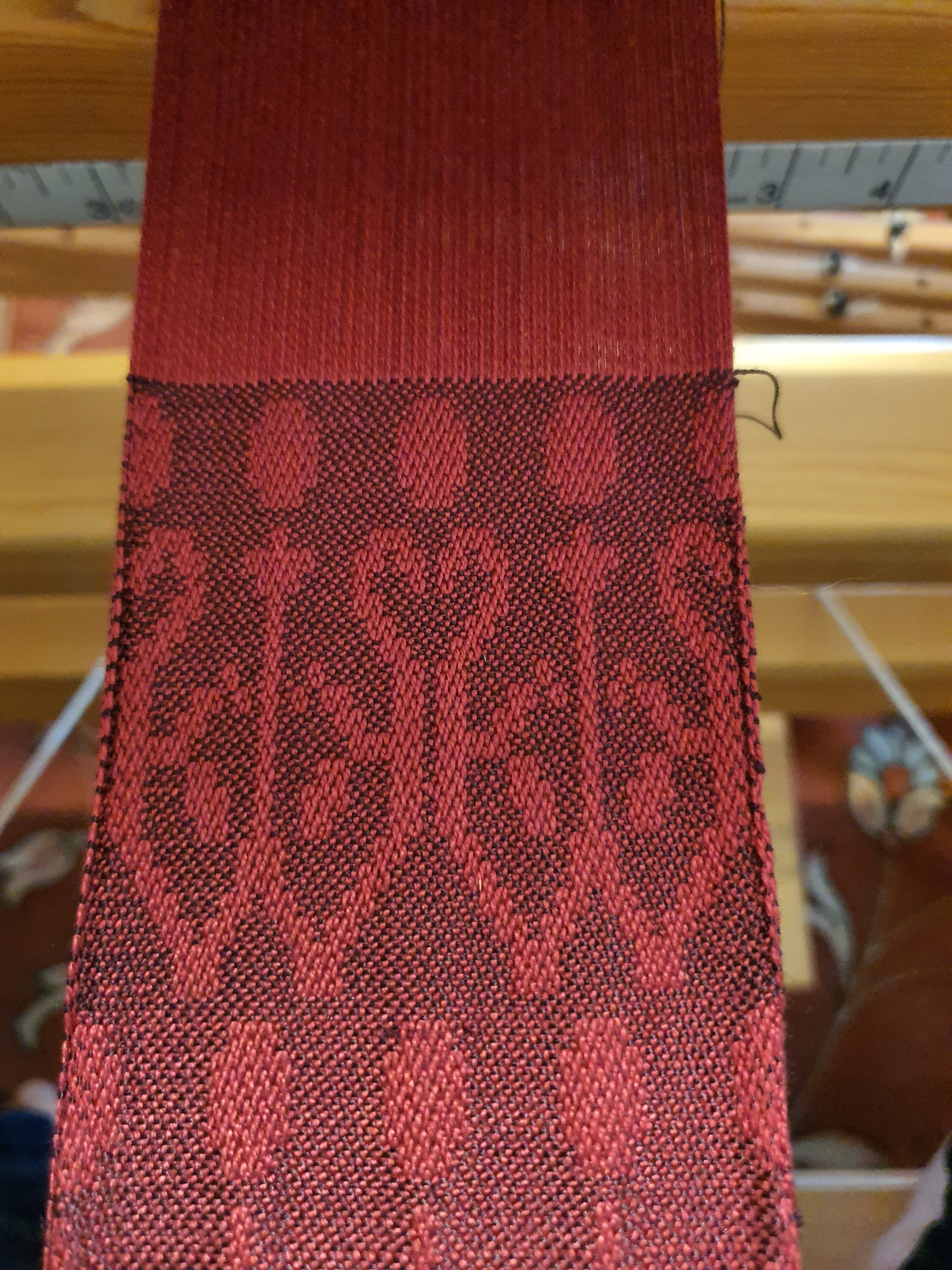A photo of red silk cloth woven in damask with a purple weft, the design is a pamette.
